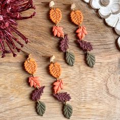 four pairs of earrings with leaves hanging from them on top of a wooden table next to dried flowers