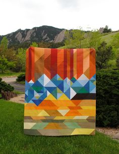 the welcome to colorful colorado quilt is displayed in front of a grassy area with mountains and trees