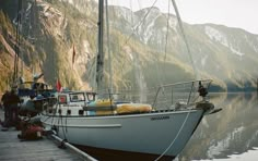 a sailboat docked at a pier with mountains in the background and people standing on it