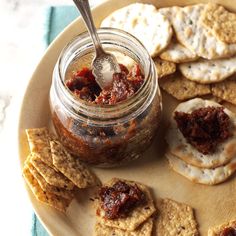 a plate with crackers and jam on it next to a jar filled with jelly