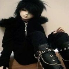 a doll sitting on top of a wooden table next to black boots and chain bracelets