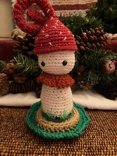 a crocheted snowman sitting on top of a table next to pine cones