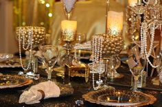 a table topped with lots of gold and white plates covered in crystal beads next to candles