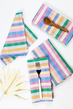 colorful striped napkins and fork on white surface with palm leaf next to them for decoration