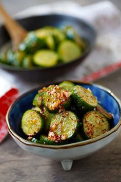 a bowl filled with sliced cucumbers on top of a wooden table next to another bowl