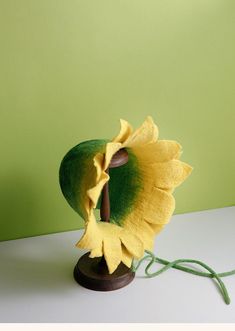 a yellow and green flower on a wooden stand next to a green wall with a cord