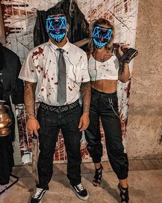 two people wearing masks and standing next to each other in front of a wall with graffiti on it