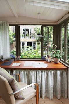 a desk with a laptop and papers on it in front of a window that looks out onto a garden