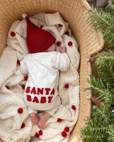 a baby is sleeping in a basket next to a christmas tree wearing a santa hat