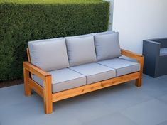 a wooden couch sitting next to a green hedge