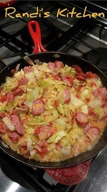 sausage and cabbage cooking in a skillet on top of the stove with a red spatula