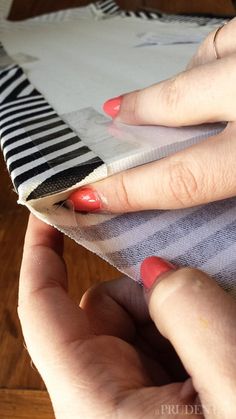 a woman's hands with red nail polish on top of a piece of fabric