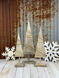 three wooden christmas trees sitting next to each other on top of a white table covered in snowflakes