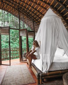 a woman sitting on top of a bed in a room with wooden floors and walls