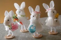 four little white rabbits dressed in dresses and holding flowers, standing next to each other