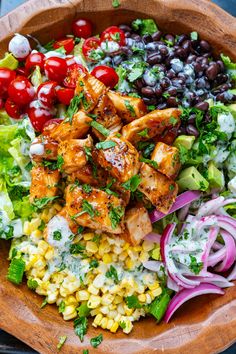 a wooden bowl filled with chicken, corn, and salad next to black olives