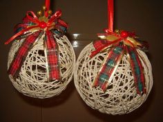 two white christmas balls with bows hanging from strings on the wall next to each other