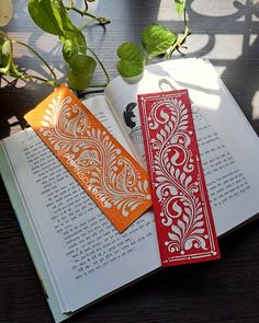 two bookmarks sitting on top of an open book next to a potted plant