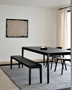 a black table and bench in a white room with a large painting on the wall