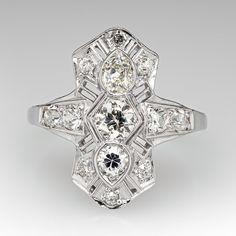 This elegant circa 1920s ring features a pierced design and is bordered with milgrain edging. The ring is centered with a row of three (3) old European/old mine cut diamonds bead set into hexagonal and pear shaped settings. The center diamonds are bordered with nine (9), bead set, old European cut diamonds and one (1), bead set, round brilliant cut diamonds. The ring measures 20.8mm at the top, rises 4.3mm above the finger, tapering to 1.8mm wide and 0.9mm thick at the base of the shank. This ring is currently a size 7.25. Art Deco Diamond Ring With Prong Setting, White Gold Diamond Ring With Milgrain Detail, Heirloom Diamond Rings With Milgrain Detail, Classic Formal Diamond Ring With Milgrain Detail, Estate Platinum Diamond Ring With Diamond Cut, Classic Milgrain Diamond Ring For Formal Occasions, Formal Art Deco Cluster Ring, Estate Style Diamond Rings With Accents, Art Deco Diamond Ring With Accents For Vintage Events