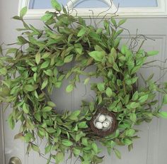 a wreath with an egg in it hanging on the front door, next to a bird's nest