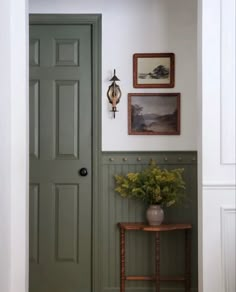 an entryway with a green door and potted plant on the table next to it