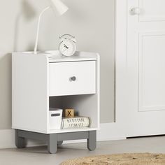 a white nightstand with a clock and books on it in a room next to a door