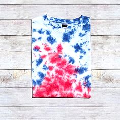 a red, white and blue tie - dyed t - shirt hanging on a wooden wall