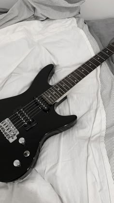 a black electric guitar laying on top of a bed