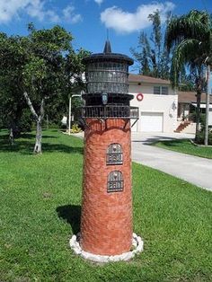 a red brick lighthouse sitting in the middle of a lush green field next to a house