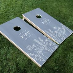 two cornhole game boards sitting on top of green grass with white flowers painted on them