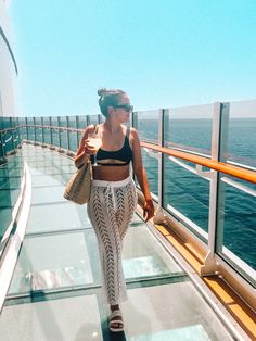 a woman walking down a walkway next to the ocean on a cruise ship with her hand in her pocket