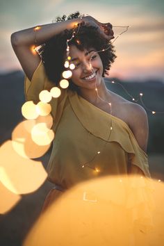 a woman in a yellow dress smiles as she holds her hair back with string lights around her