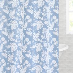 a blue shower curtain with white flowers on it in front of a tub and window