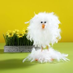 a fake white bird sitting on top of a table next to some flowers and grass