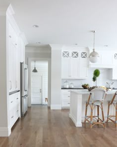 an open kitchen with white cabinets and wood flooring, along with two bar stools