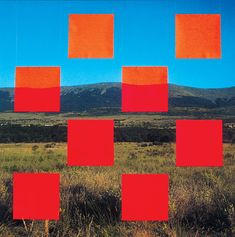 red squares are arranged in the middle of an open field with mountains in the background