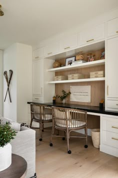 an office with white cabinets and black counter tops, along with two wicker chairs