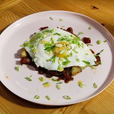 a white plate topped with an egg and bacon hashbrowns covered in green onions