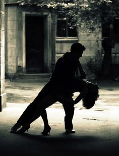 a man and woman are dancing in an alleyway at night, one is holding the other's head