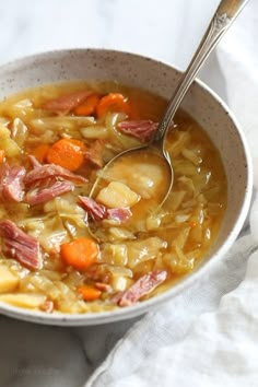 a white bowl filled with ham and cabbage soup on top of a table next to a napkin