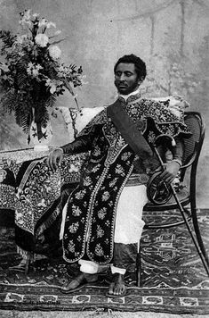 an old black and white photo of a man sitting on a chair with flowers in his lap