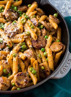 a skillet filled with pasta, peas and sausages on top of a blue towel