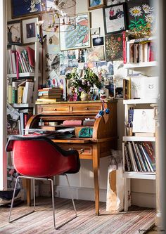 a red chair sitting in front of a desk with books on the wall behind it