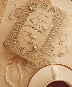 an antique book, bracelets and ring are on the table next to a cup of coffee