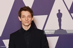 the actor is posing in front of an oscars backdrop and wearing a black suit