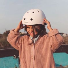 a woman wearing a white helmet while standing next to a skateboard