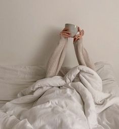 a person laying in bed holding a cup