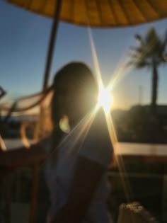 a woman standing under an umbrella with the sun behind her