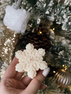 a hand holding a snowflake ornament in front of a christmas tree